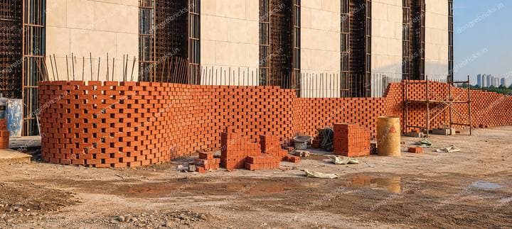 Curved perforated brick wall under construction with brick stacks on site