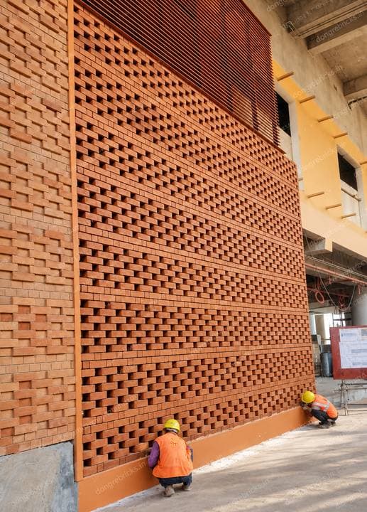 Large perforated brick screen wall under construction, workers for scale